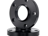 A black metal flange with multiple bolt holes is stacked on another flange. The top flange is elevated, showcasing its circular shape in a plain white background.