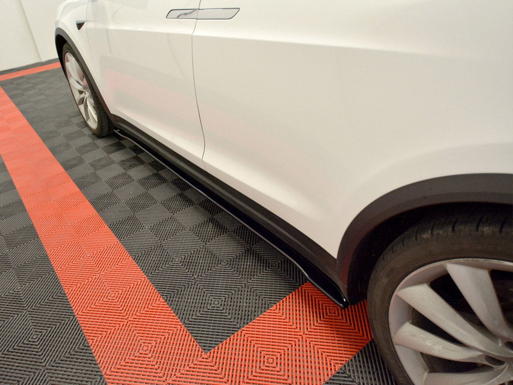 A white car is parked, showcasing its side and wheel, on a black and red checkered garage floor, providing a visually striking contrast.