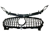 A black car grille with horizontal and vertical chrome accents lies on a white background, featuring a central circular emblem space and attached frame components.