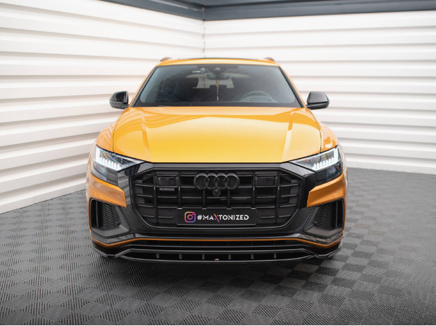Yellow Audi SUV parked inside a bright, white-paneled garage with black flooring. The front grille is prominent. Visible text: "GMS," "CC2069," and "MAXTONIZED" on the license plate area.