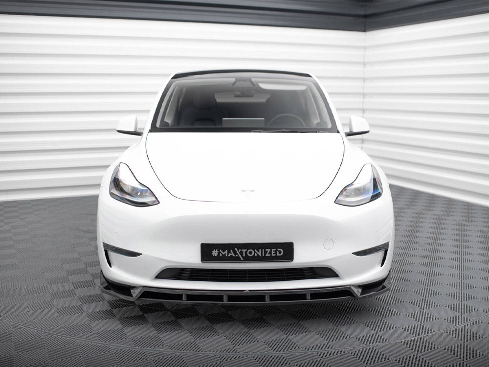 A white car is parked in a corner of a room with white and gray walls and flooring. The license plate reads "#MAXTONIZED."