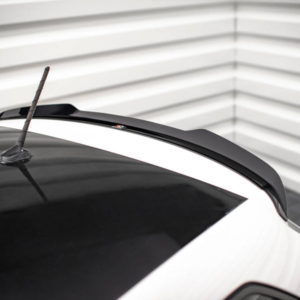 A car roof with a black roof spoiler and aerial, set in a corner with white horizontal wall panels.