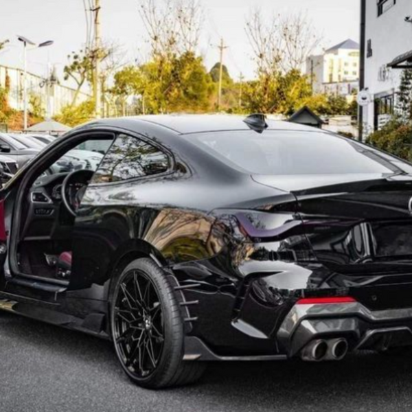 A sleek black car with an open driver's door revealing a red interior is parked on a street, surrounded by trees and modern buildings.