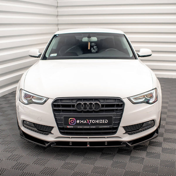 A white car faces forward in a well-lit, enclosed space with patterned flooring. Its license plate reads "INSTAGRAM #MAXTONIZED" and displays the Audi logo prominently on the grille.