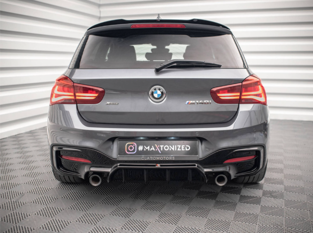 A gray BMW car, positioned stationary, displays dual exhausts and illuminated tail lights in a well-lit showroom. Text: "X Drive," "M140i," and "#MAXTONIZED" with "CLAIRMOTORS."