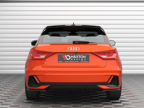 An orange Audi A1, parked on a checkered floor, faces a white garage door. The rear displays the logo and "Maxton Design" on the license plate area.