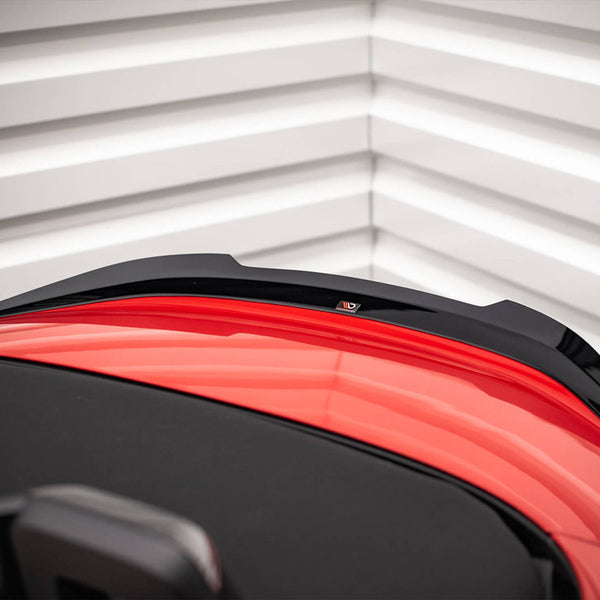 A red sports car's rear end with a black aerodynamic spoiler is parked against a textured white garage door with horizontal lines.