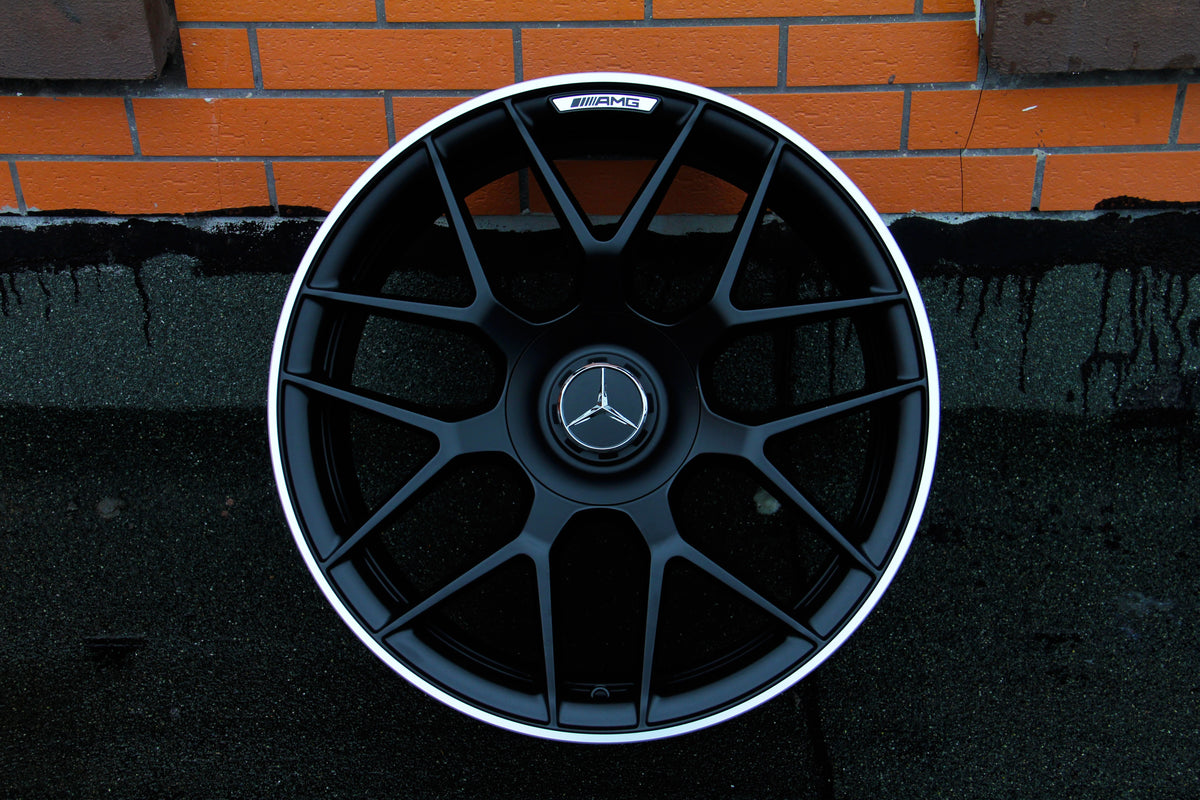 A black alloy wheel, featuring a Mercedes emblem and "AMG" branding, rests against an orange brick wall with dark mortar.