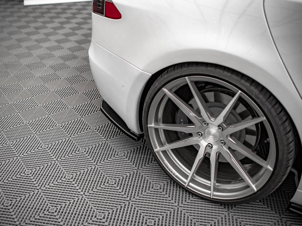 A white car is parked, showcasing its sleek, large alloy wheel on a patterned grey floor, emphasizing the vehicle's sporty design and modern environment.