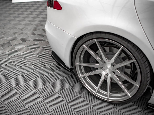 A white car is parked, showcasing its sleek, large alloy wheel on a patterned grey floor, emphasizing the vehicle's sporty design and modern environment.