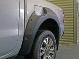 A silver pickup truck's rear wheel, equipped with a fender flare, is parked on a dark floor in front of a large, closed green garage door.