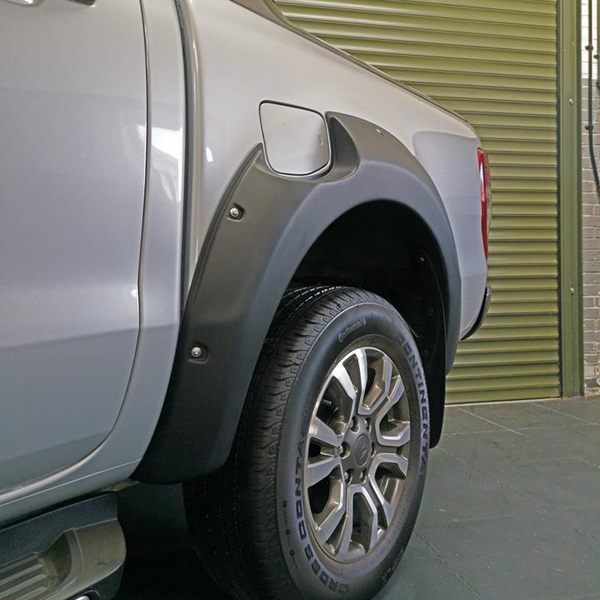 A silver pickup truck's rear wheel, equipped with a fender flare, is parked on a dark floor in front of a large, closed green garage door.