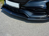 The front bumper of a sleek, black car with intricate vents and a glossy finish sits on a sunlit asphalt road. Text: 