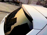Car rear window reflects urban sunset; rooftop spoiler above, parking lot and bicycle against a concrete wall in the background.