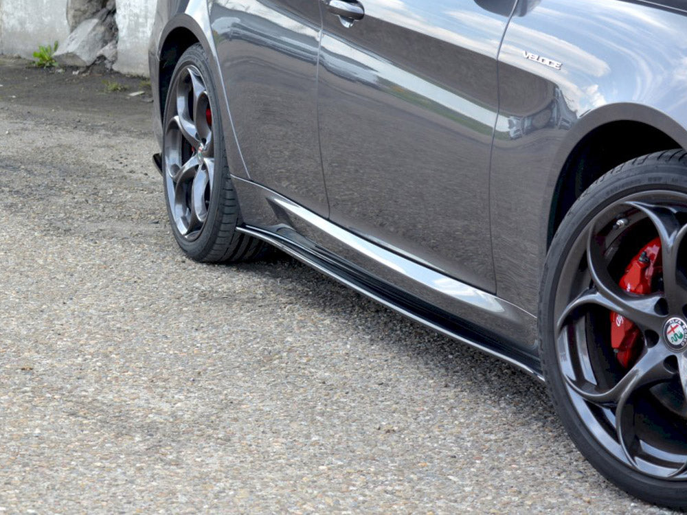 A gray car with a "Veloce" badge and red brake calipers, parked on rough pavement near concrete walls, showcasing sleek aerodynamic side panels and reflective alloy wheels.