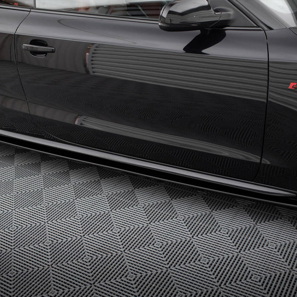 A shiny black car door with reflections parked on a patterned grey floor. The car features a red emblem and sleek design lines.