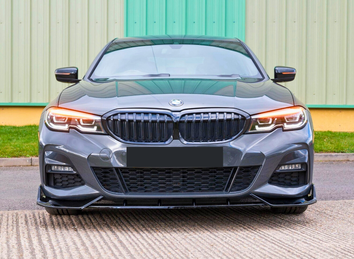 A gray BMW car is parked on a concrete surface, facing forward, in front of a green and yellow metal building. Its headlights are on, and the logo is visible.