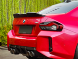 A red sports car with a visible quad exhaust system and a rear spoiler is parked on a paved surface, adjacent to a wall covered with vertical greenery. Text: 