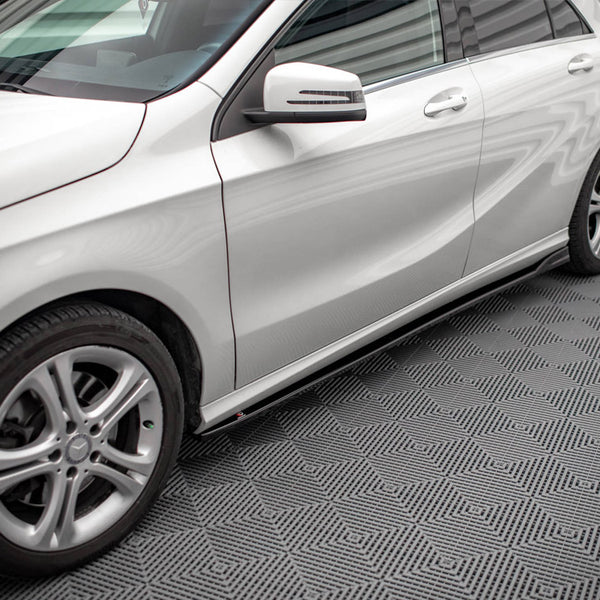 A silver car is parked on a patterned floor, displaying sleek design lines and alloy wheels. The setting has bright lighting and a textured surface, enhancing the vehicle's shine.