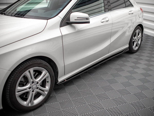 A silver car is parked on a patterned floor, displaying sleek design lines and alloy wheels. The setting has bright lighting and a textured surface, enhancing the vehicle's shine.