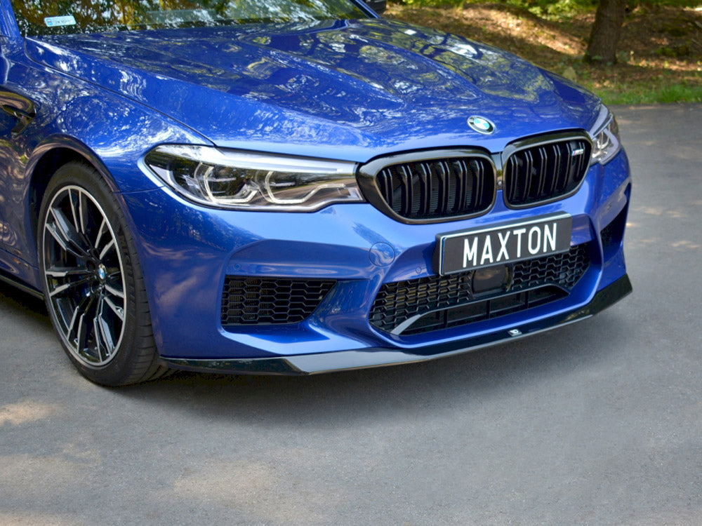 A blue car with a black grille and "MAXTON" license plate is parked on a paved road, surrounded by trees.