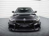 A sleek black BMW M2 faces forward, parked on a patterned floor in a bright room. The number plate reads 