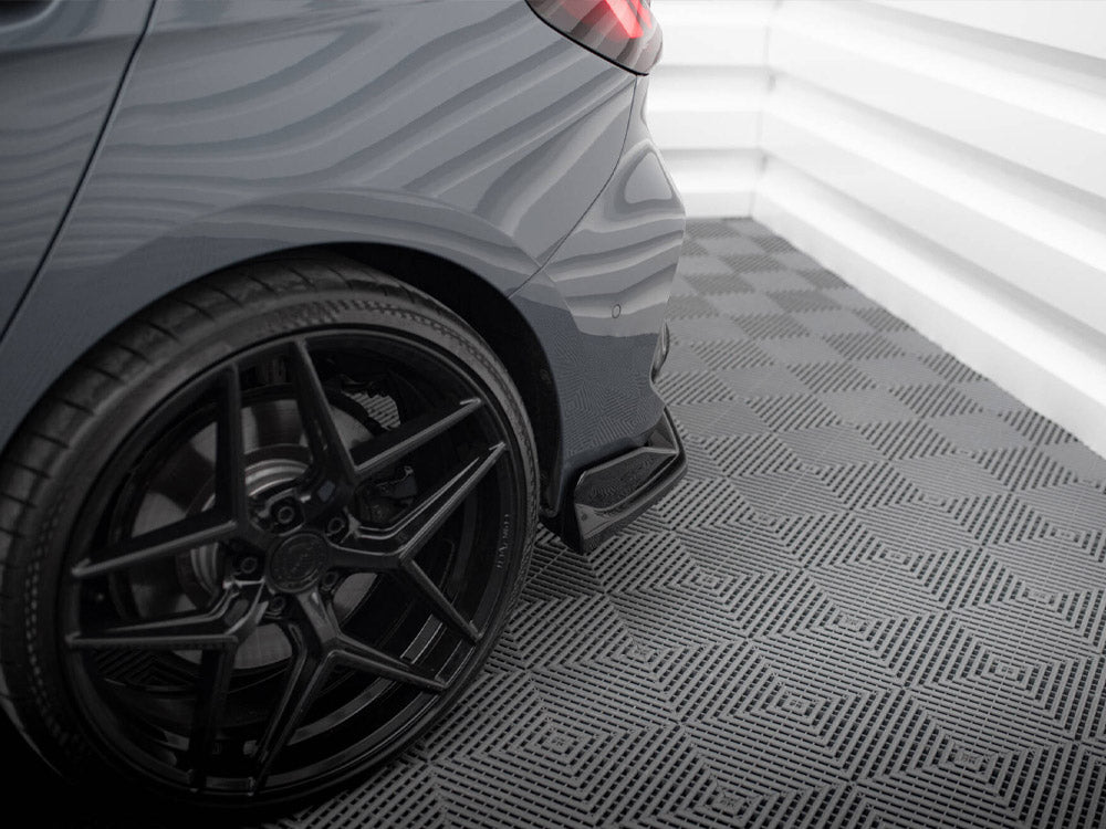 A car's rear tire and wheel resting on a patterned floor, in a brightly lit, white-walled indoor space. The environment is clean and modern, emphasizing the car's sleek design.