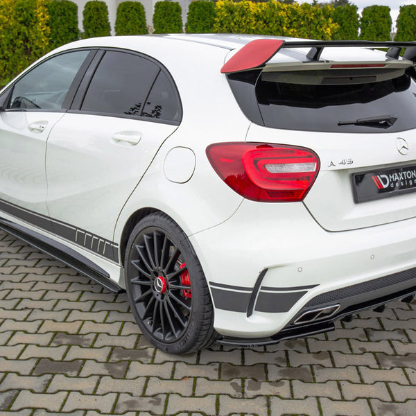 White Mercedes-Benz A45 AMG with a rear spoiler and black alloy wheels parked on a paved driveway. Background features neatly trimmed green hedges. License plate reads "MAXTON design."