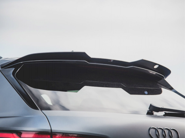 A sleek car rear spoiler extends over the tinted back window of a gray vehicle, with the Audi logo visible, set against a cloudy sky.