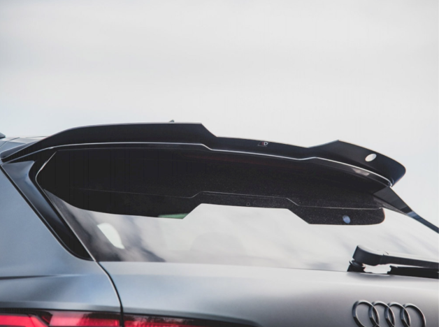 A sleek car rear spoiler extends over the tinted back window of a gray vehicle, with the Audi logo visible, set against a cloudy sky.