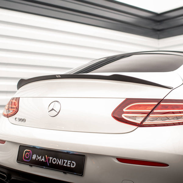 A white Mercedes-Benz C 300 is parked indoors, showcasing its rear with sleek taillights and a spoiler. The environment includes white paneled walls. The license plate reads "#MAXTONIZED".