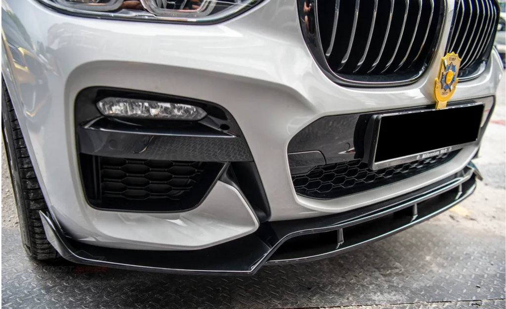Car front bumper with a sleek design, featuring a detailed grille and a decorative emblem. The vehicle is parked on a metal-patterned surface, suggesting an outdoor or garage setting.