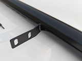 A black metal rod with two bracket holes protrudes from its side, resting on a white surface with shadowy reflections.