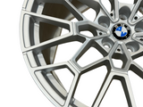 A silver alloy wheel displaying a multi-spoke design with a central BMW logo, photographed against a plain background, highlighting its detailed structure and sleek metallic finish.