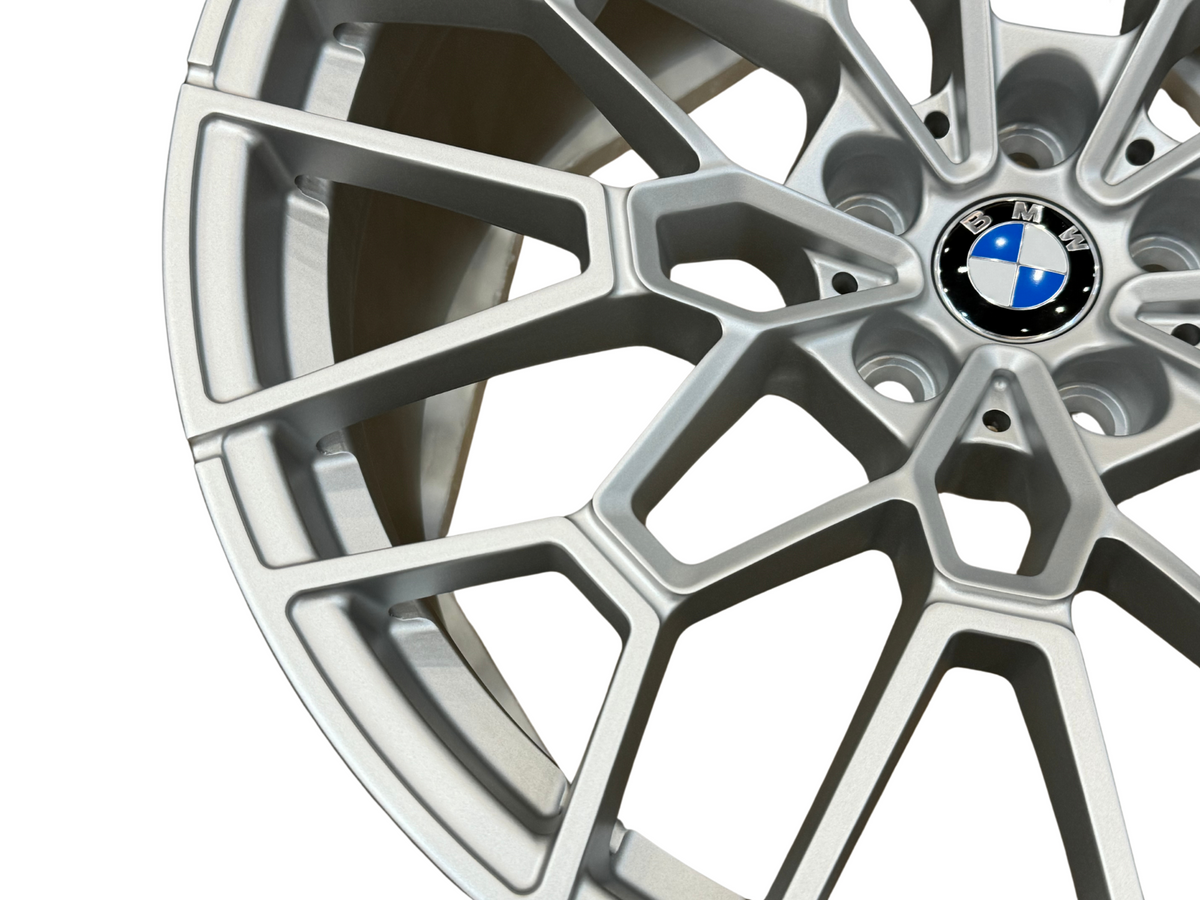 A silver alloy wheel displaying a multi-spoke design with a central BMW logo, photographed against a plain background, highlighting its detailed structure and sleek metallic finish.