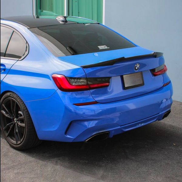 A blue car is parked near a light blue building. The car's rear features dual exhausts and dark-tinted windows. "BMW" and "3DDesign" are visible on the rear window.