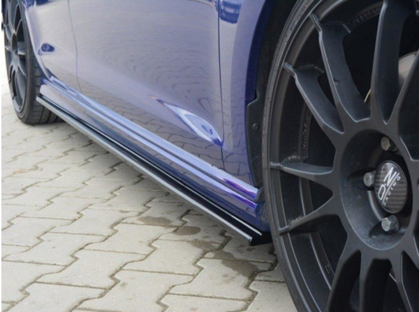 A blue car with black alloy wheels is parked on a stone pavement. The car features Oz Racing wheels and visible side skirts reflecting light.