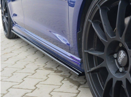A blue car with black alloy wheels is parked on a stone pavement. The car features Oz Racing wheels and visible side skirts reflecting light.