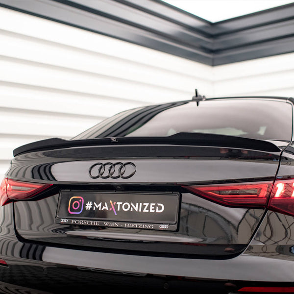 A black Audi car is parked indoors, facing away. The taillights are illuminated, and the license plate reads "#MAXTONIZED Porsche Wien Hietzing." The setting has white panel walls.
