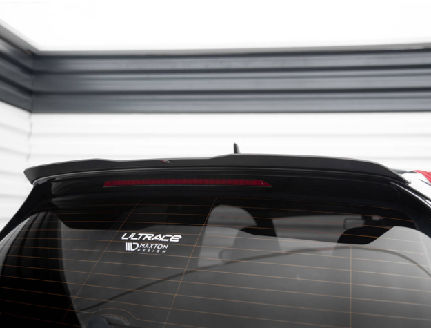 A car rear window with a high-mounted brake light displays two stickers reading "ULTRACE" and "Maxton Design." It's parked against a wall with horizontal black and white stripes.