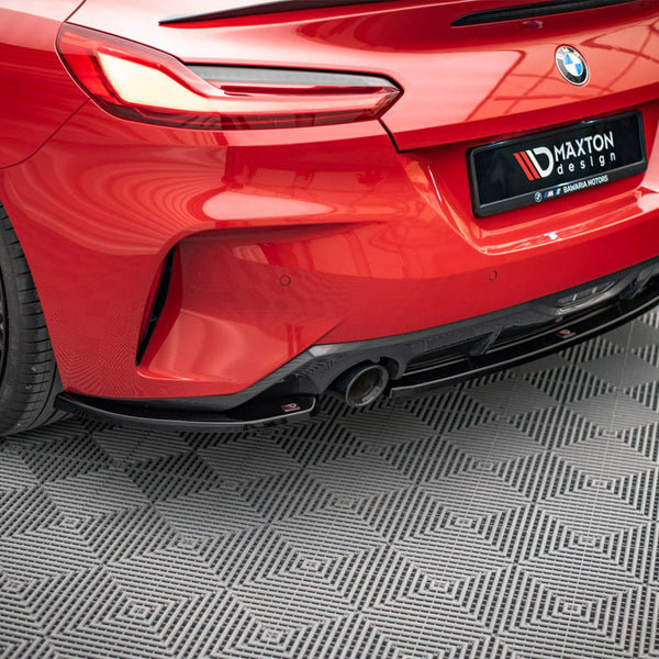 A red BMW car's rear, featuring sleek taillights and a dual exhaust, is parked on a patterned floor. The license plate reads "MAXTON design ✯ BAVARIA MOTORS."