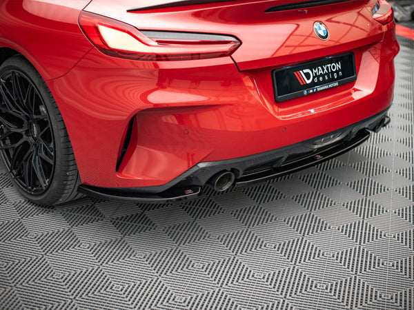 A red BMW car's rear, featuring sleek taillights and a dual exhaust, is parked on a patterned floor. The license plate reads "MAXTON design ✯ BAVARIA MOTORS."