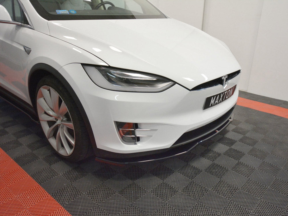 A white Tesla car is stationary, showcasing a front view on a black-and-red checkered floor. The license plate reads "MAXTON."