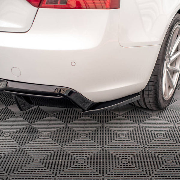 A white car's rear bumper and wheel are shown on a textured, gray, diamond-patterned floor. The car features a black diffuser underneath the bumper, adding sporty detailing.