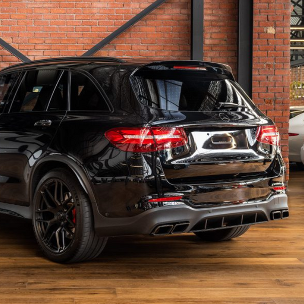 A black SUV is parked indoors on a wooden floor, with brick walls and industrial beams surrounding it. Other vehicles are visible in the background.