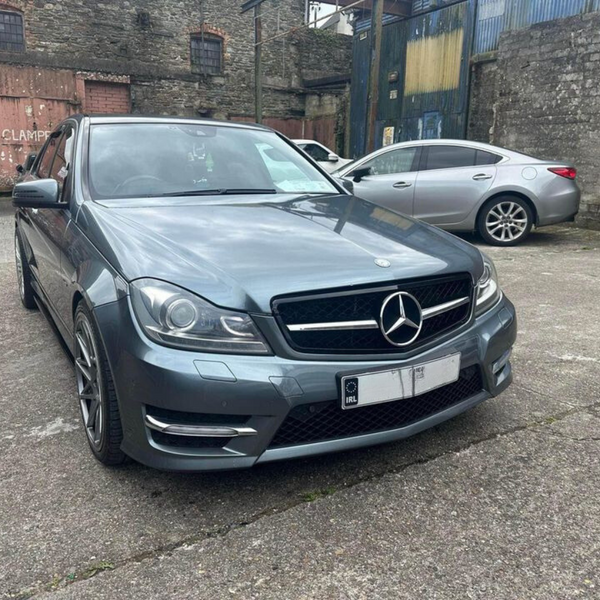 A silver Mercedes-Benz is parked in an industrial yard next to two other cars. The surrounding environment features stone walls and a metal structure with a sign: "CARS WILL BE CLAMPED."