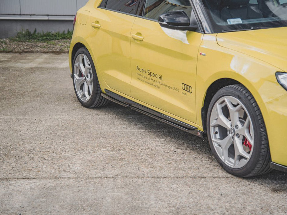 A yellow Audi car is parked on a concrete surface. The side displays: "Auto-Special" with contact details and the Audi logo. A building and grass are visible in the background.