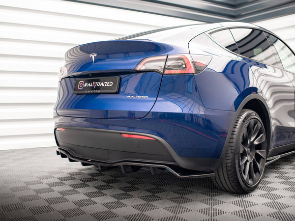 A blue Tesla Model Y with "Dual Motor" label is parked, showing its sleek rear against a patterned floor. The license plate reads "#MAXTONIZED TESLA.COM".