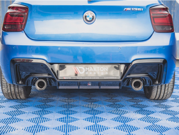 A blue BMW M135i is parked on a blue patterned floor with visible dual exhausts. The license plate reads "MAXTON design."