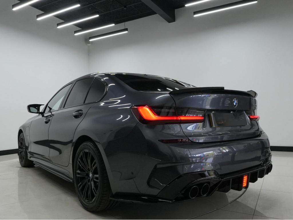 A dark gray car with tinted windows is parked in a well-lit room, showcasing sleek tail lights and a prominent rear bumper design.